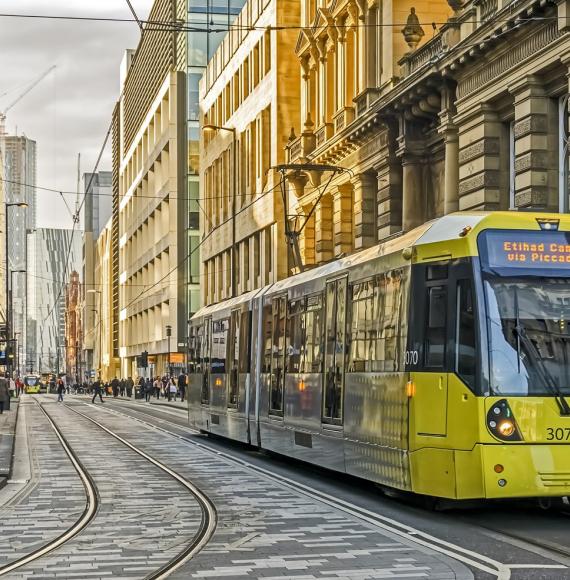 View of Manchester city centre, UK. A tram can be seen approaching and people can be seen walking on the roads.