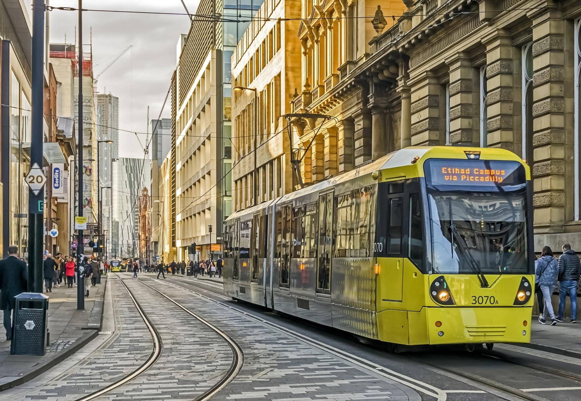View of Manchester city centre, UK. A tram can be seen approaching and people can be seen walking on the roads.