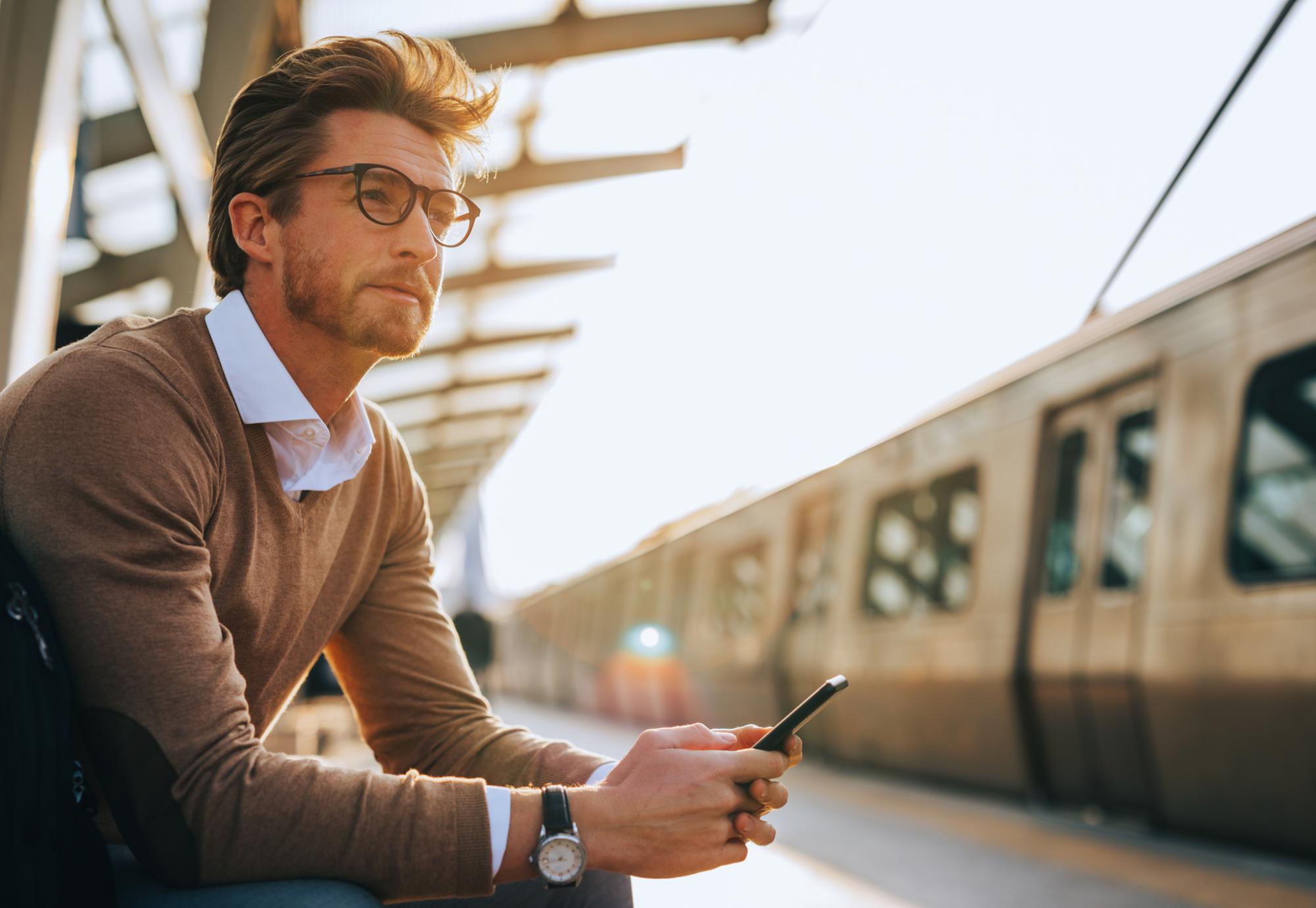 Man waiting at a train station with a phone