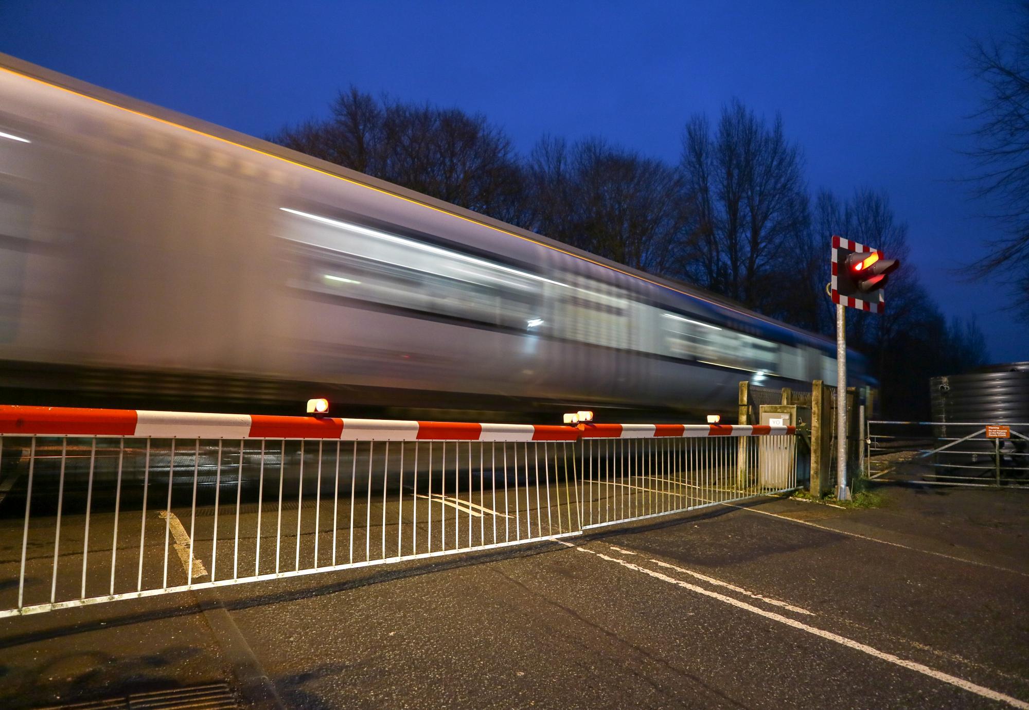 Warning lights showing and the barriers down at a level crossing as a train speeds past, via Istock 