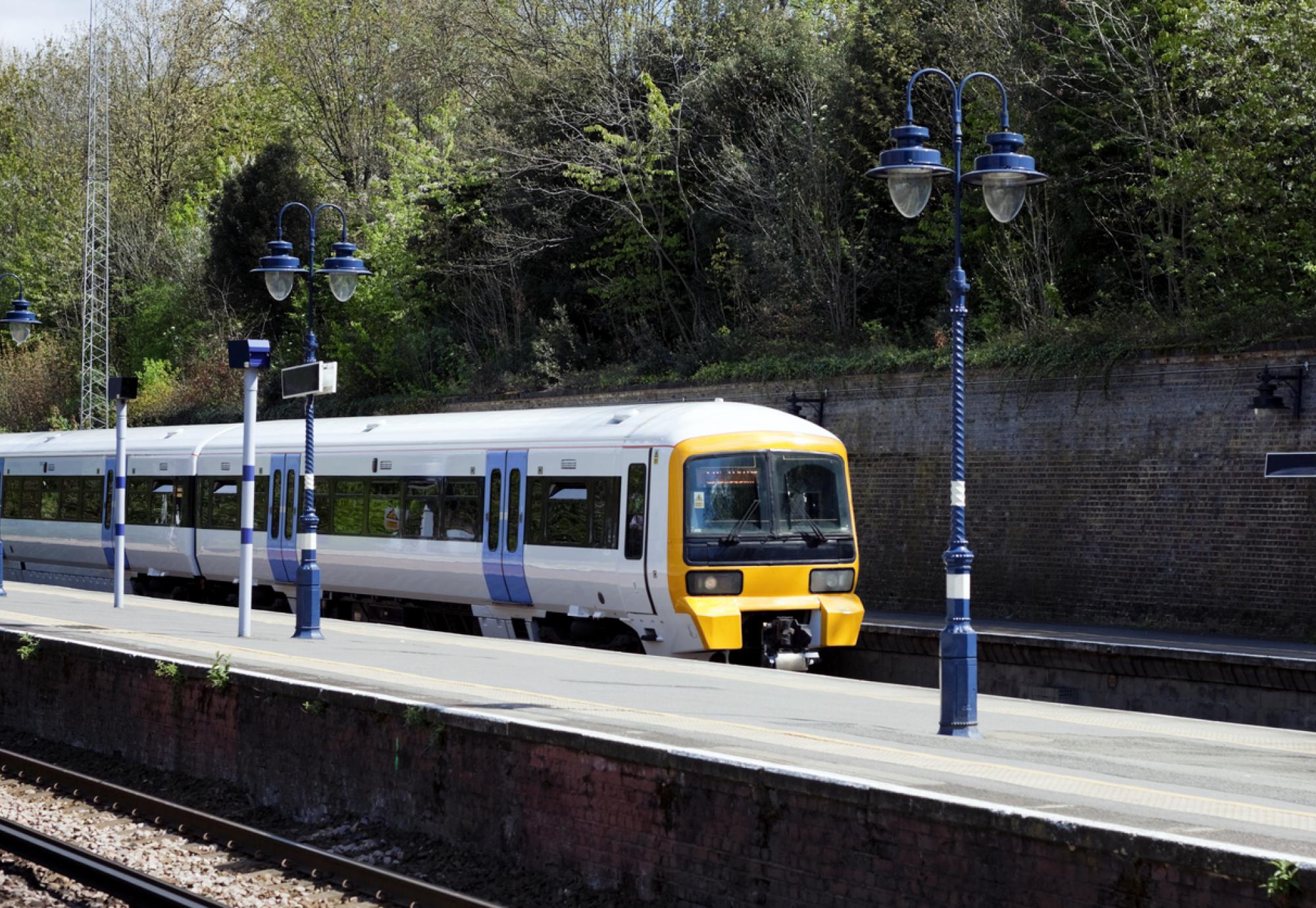 An electricity-powered passenger train entering a London suburban station on a bright and sunny April day.