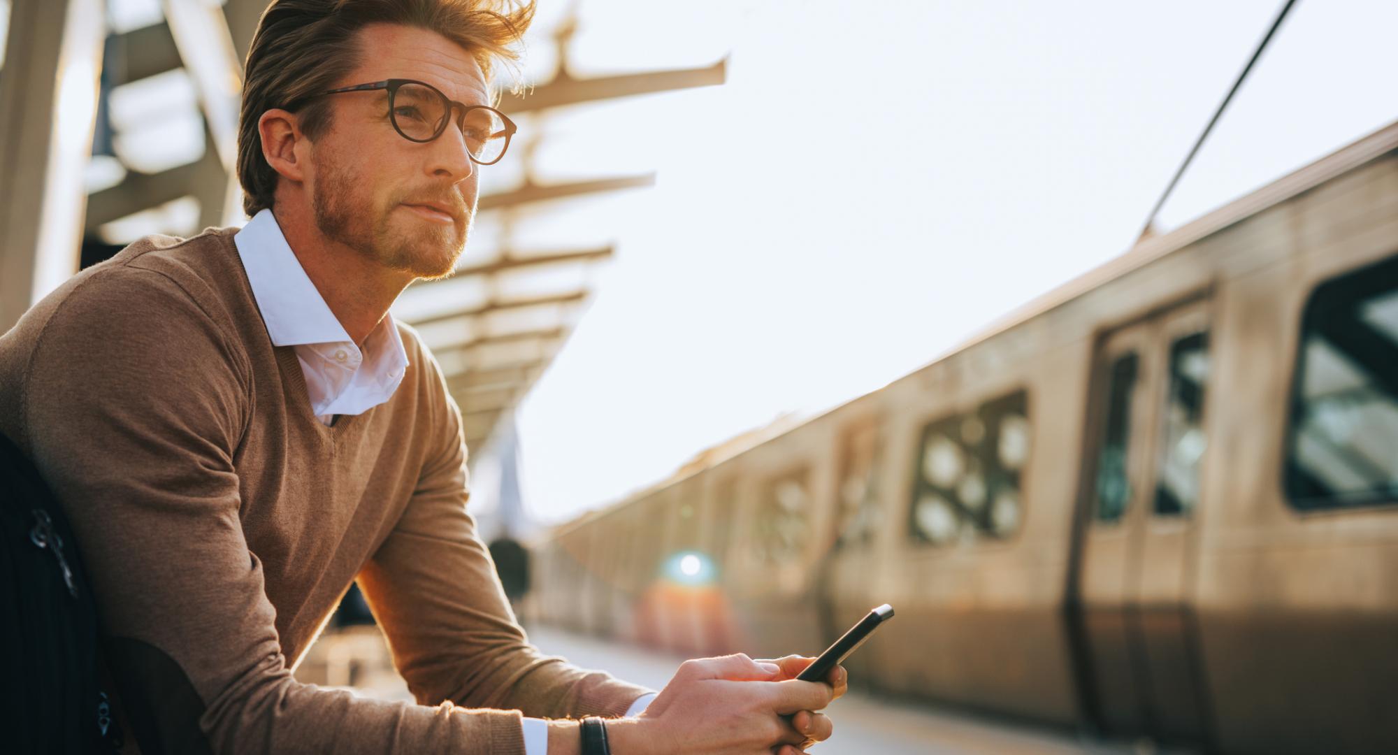 Man waiting at a train station with a phone