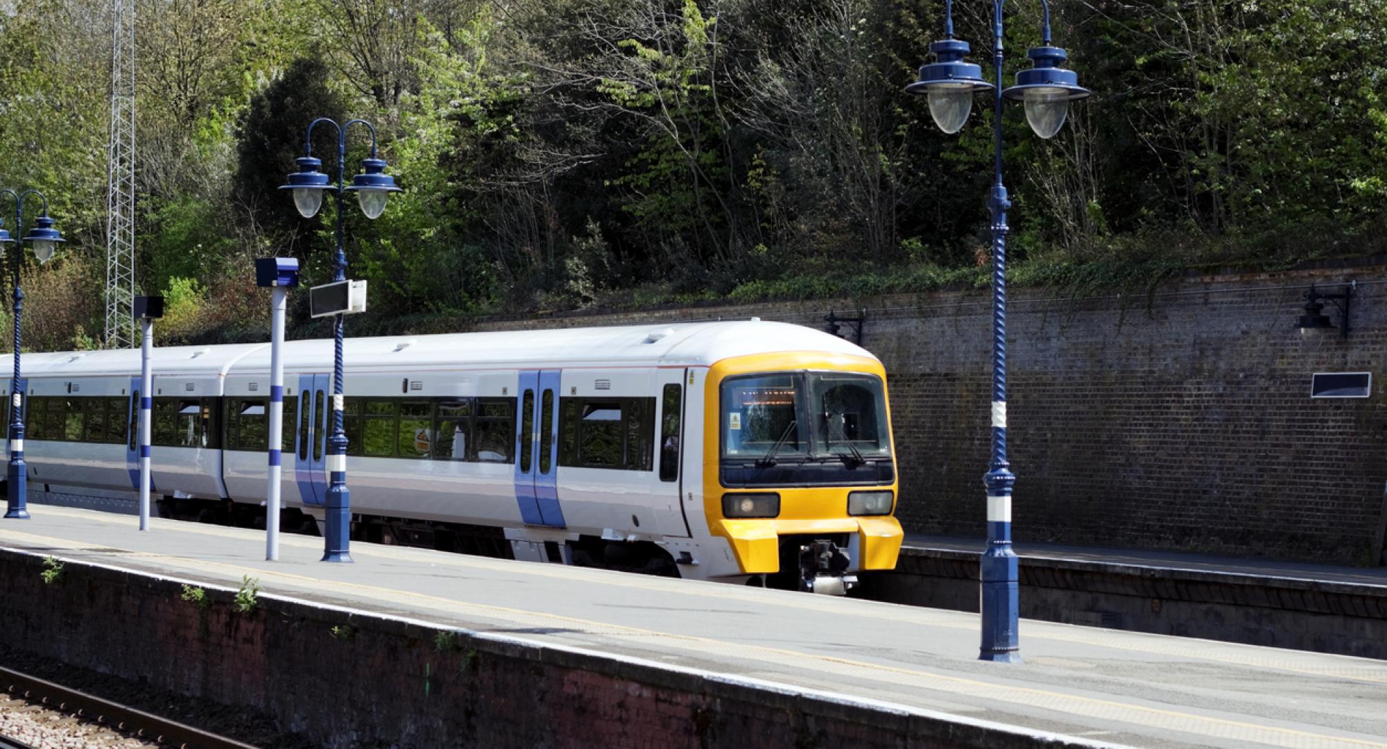 An electricity-powered passenger train entering a London suburban station on a bright and sunny April day.