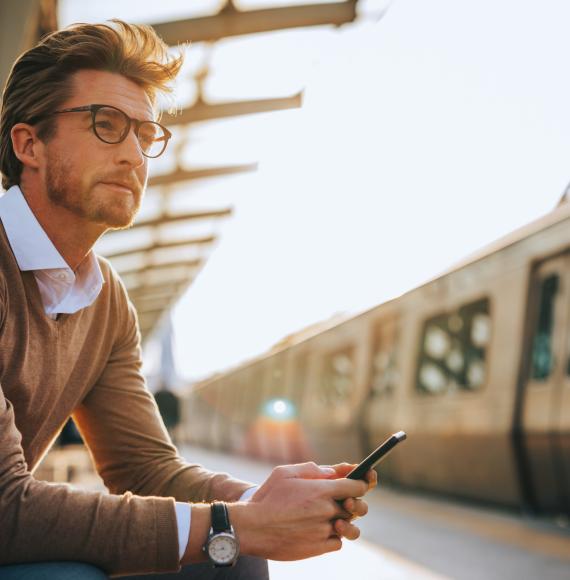 Man waiting at a train station with a phone