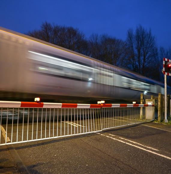 Warning lights showing and the barriers down at a level crossing as a train speeds past, via Istock 