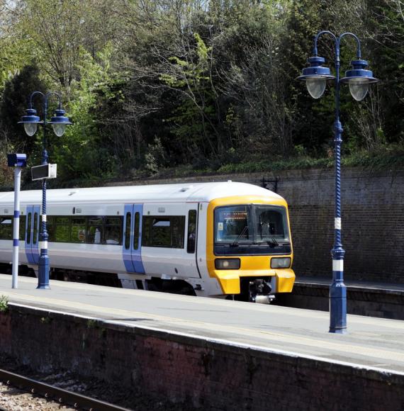 An electricity-powered passenger train entering a London suburban station on a bright and sunny April day.